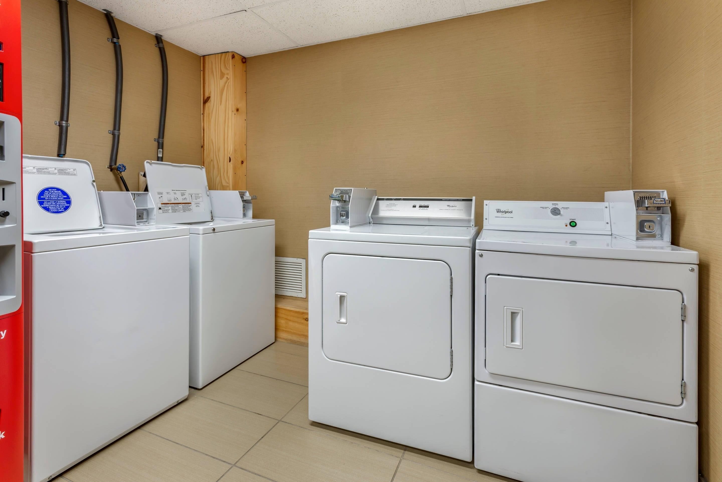 A laundry room with three stacked washers and dryers, a red water heater, and visible plumbing.
