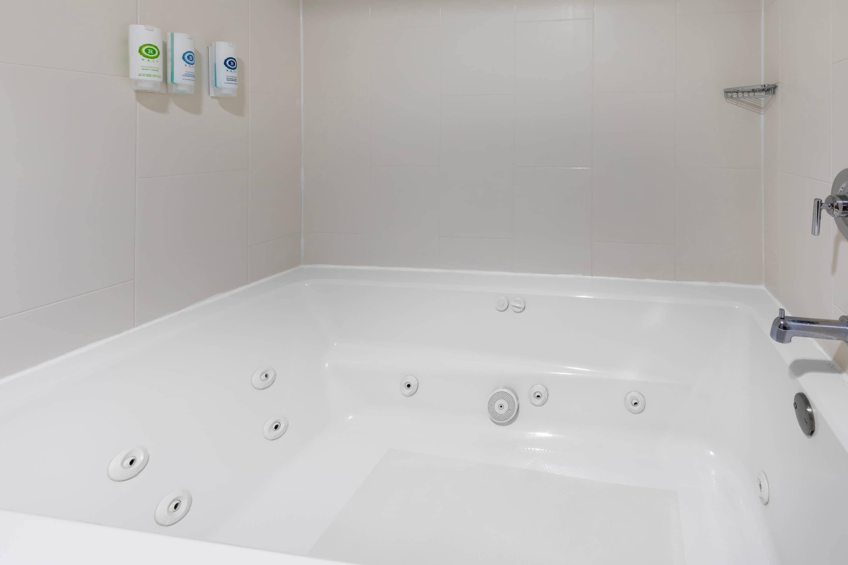 A white bathtub with multiple drain holes, a chrome faucet, and a showerhead on the right.