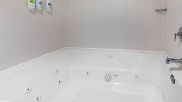 A white bathtub with multiple drain holes, a chrome faucet, and a showerhead on the right.