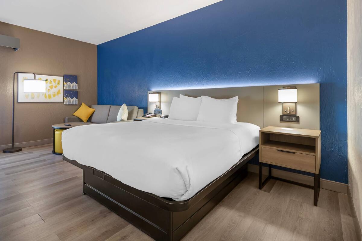 Una habitación de hotel moderna con una cama grande, mesitas de noche y una lámpara de pared.