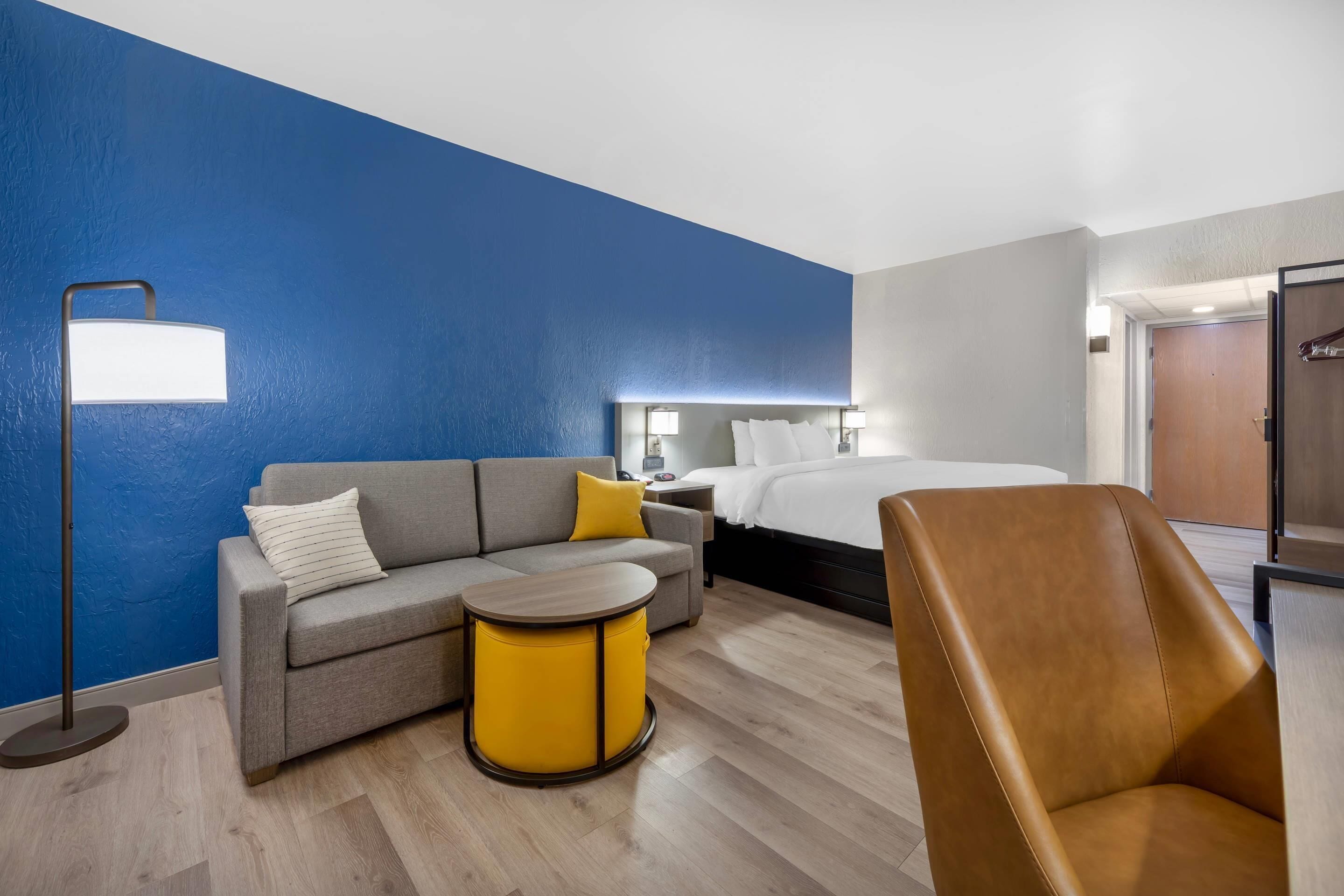A hotel room with a bed, a sofa, a chair, a small table, and a floor lamp.