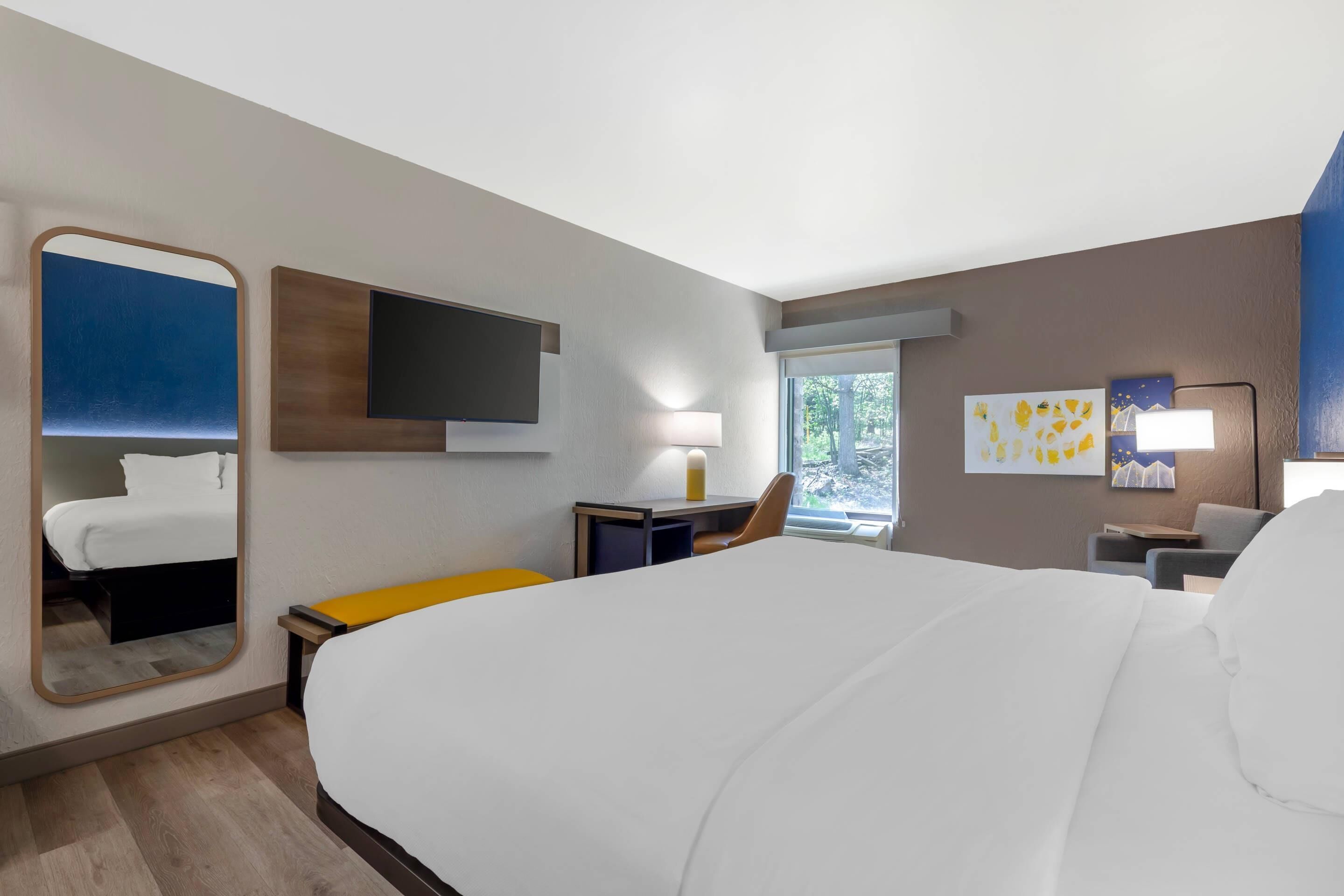 A hotel room with a large bed, a flat-screen TV, a desk with a chair, and artwork on the walls.