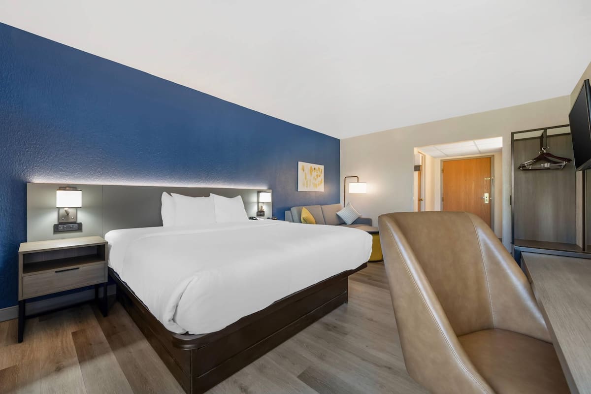 Una habitación de hotel con una cama grande, mesitas de noche con lámparas, una silla, un televisor y un armario.