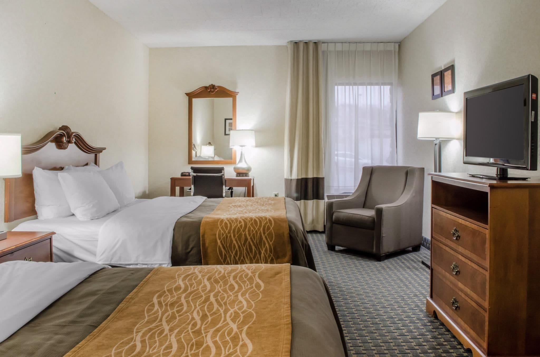 A hotel room with two beds, a desk, a chair, a television, and a dresser.