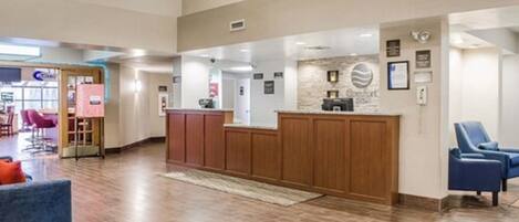 A hotel lobby with a reception desk, seating area, and a visible entrance to a restaurant.