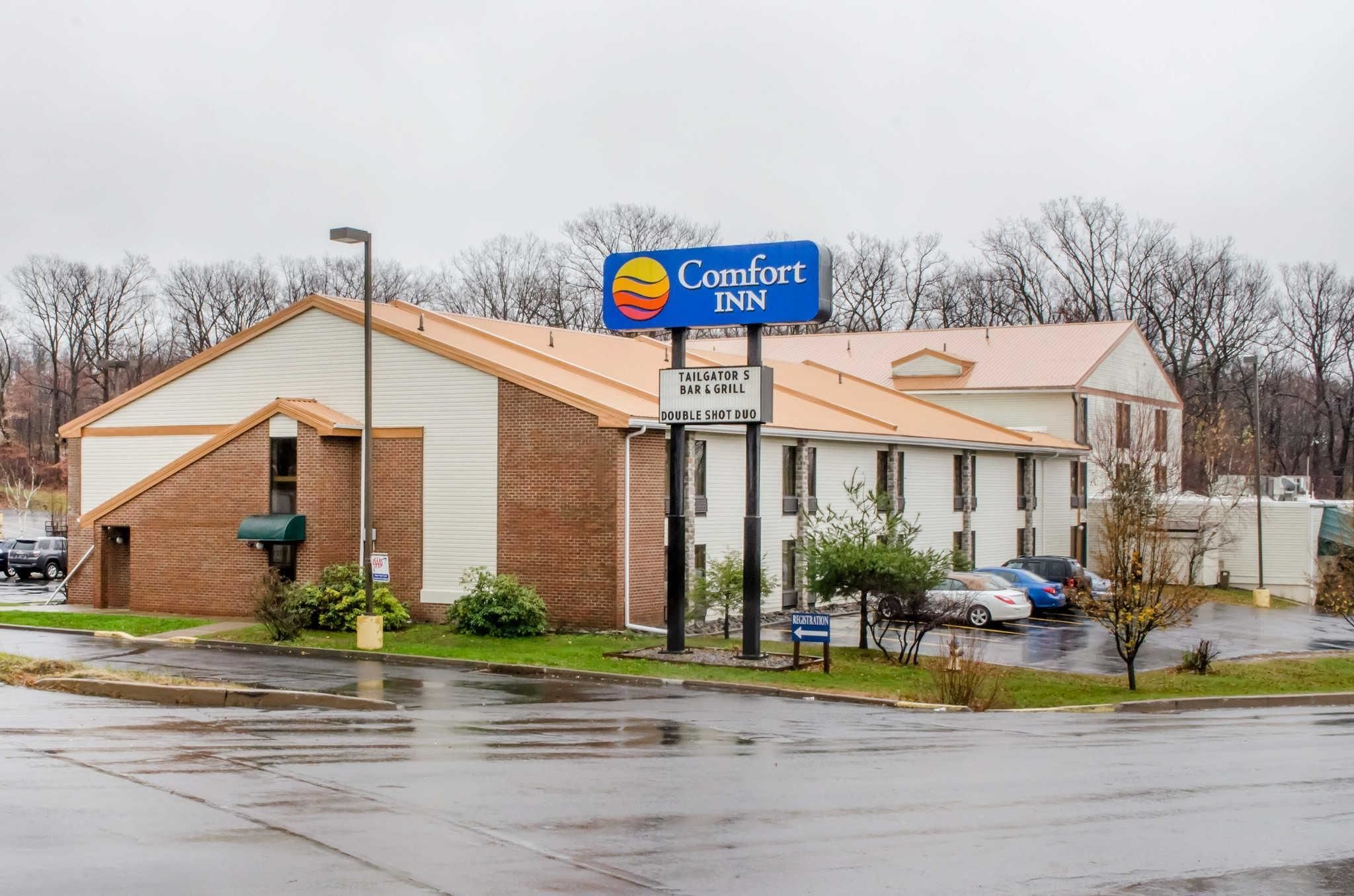 Un hotel Comfort Inn con fachada de ladrillo, un letrero de Tailgator's Bar & Grill y un estacionamiento con automóviles.