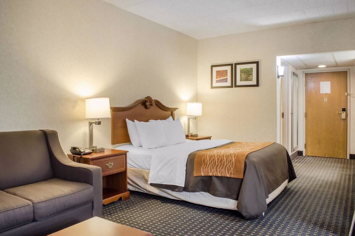 Una habitación de hotel con cama, dos lámparas de noche, una mesita de noche, un escritorio, una silla y una puerta.