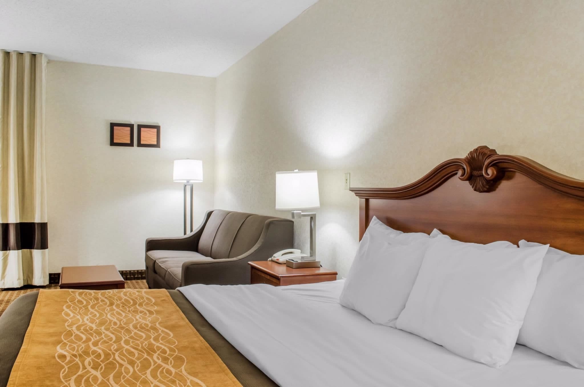 Habitación de hotel con una cama grande, un sofá, un escritorio con lámpara y una ventana con cortinas.