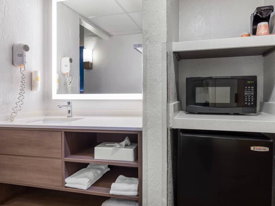 Casa de banho com lavatório, secador de cabelo, espelho, micro-ondas e frigorífico.