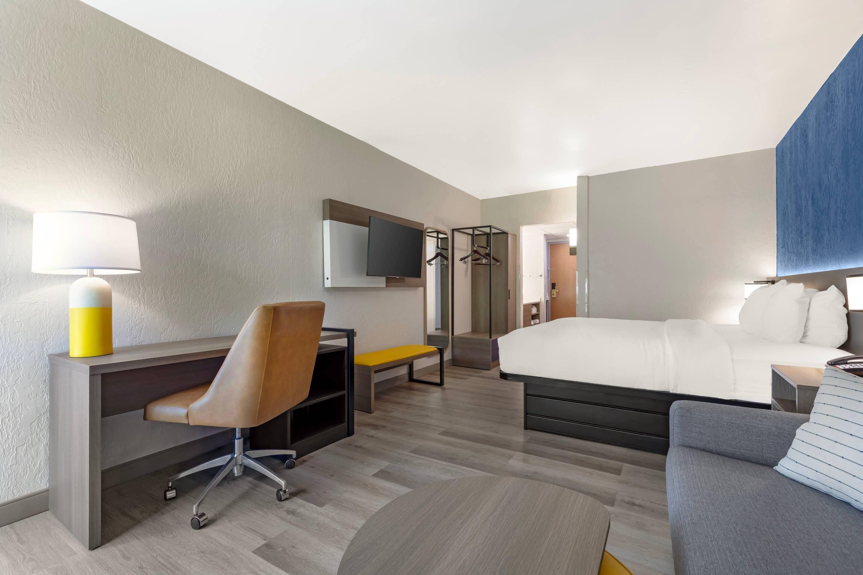 Una habitación de hotel con cama, escritorio, silla, televisor y perchero.