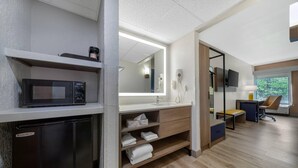Une salle de bain moderne équipée d’un four à micro-ondes encastré, d’un meuble-lavabo avec miroir et d’un coin salon comprenant un bureau et une chaise.