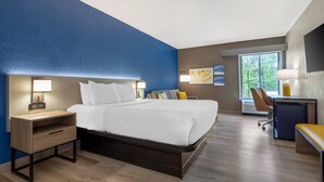 Une chambre d’hôtel moderne équipée d’un lit, d’une table de chevet, d’un bureau, d’une chaise et d’une grande fenêtre.