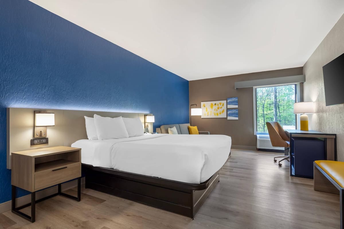 Una habitación de hotel moderna con cama, mesita de noche, escritorio, silla y un gran ventanal.