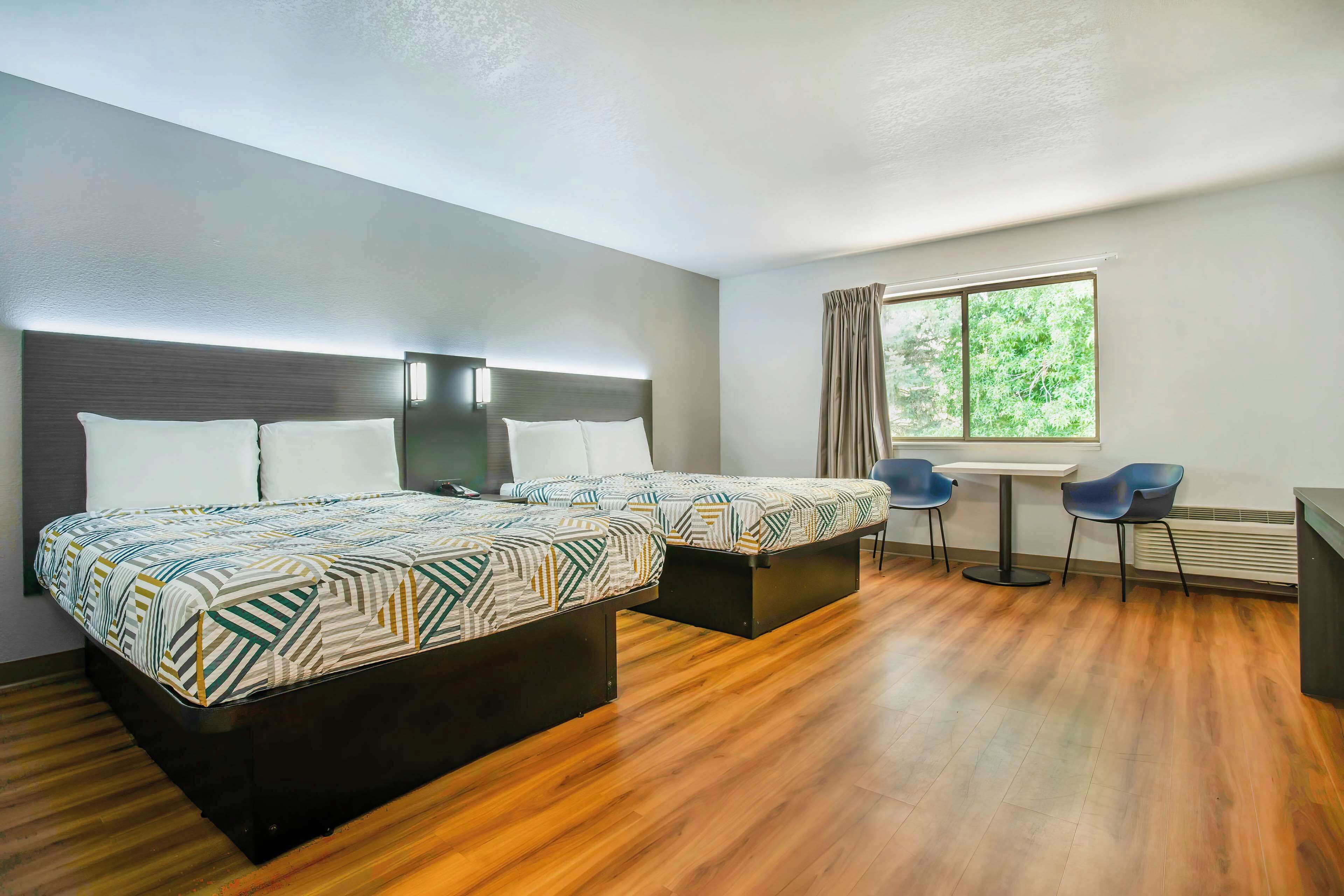 A hotel room with two beds, a desk, two chairs, and a window with curtains.