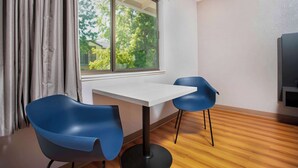 A modern room with a large window, two blue chairs, a white table, and a TV on the right. - Motel 6 Gresham, OR - Portland (Gresham)
