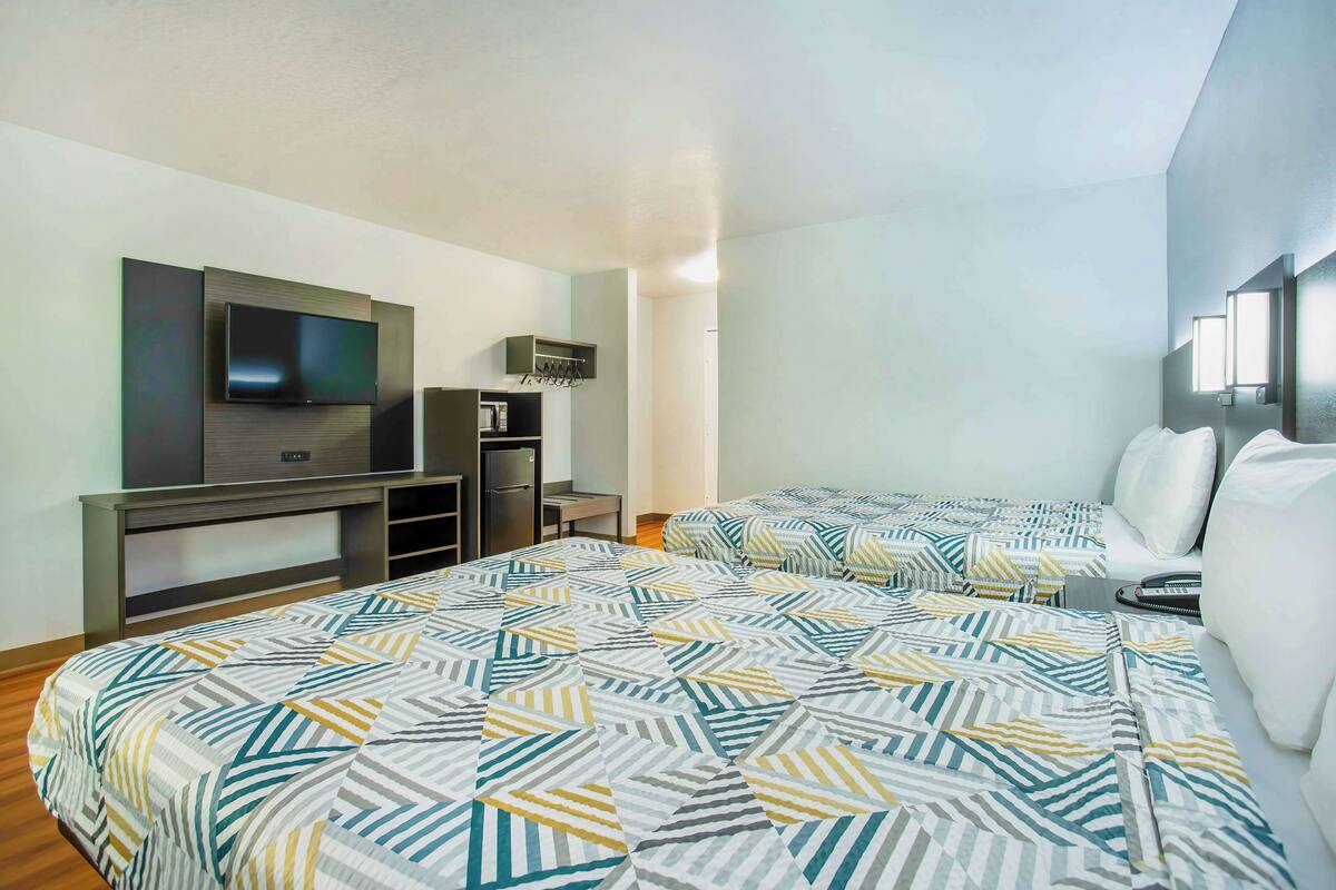 Une chambre d’hôtel équipée d’une télévision, d’un minibar, d’un bureau et de deux lits avec une literie à motifs.