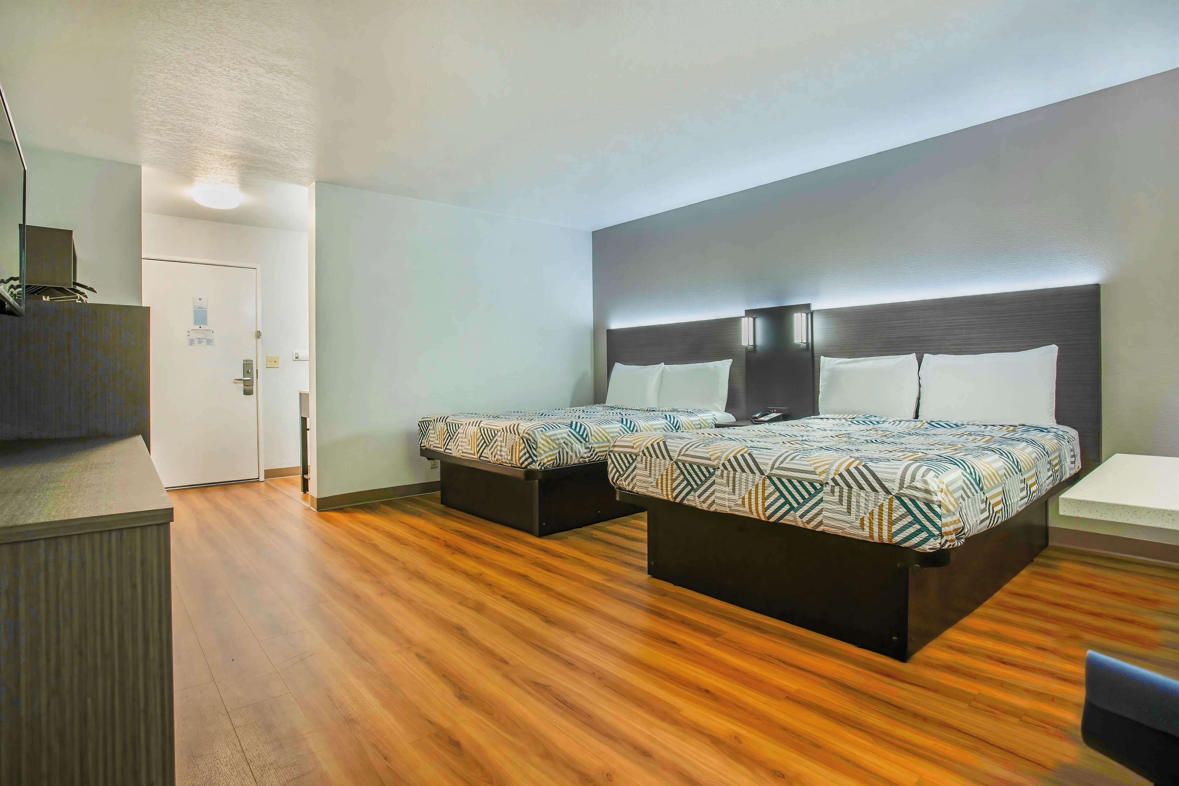Ein Hotelzimmer mit Holzboden, einem Bett mit gemusterten Bettwaren, einem Nachttisch und einem Schreibtisch mit Stuhl.