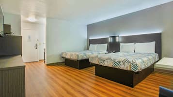 Ein Hotelzimmer mit Holzboden, einem Bett mit gemusterten Bettwaren, einem Nachttisch und einem Schreibtisch mit Stuhl.