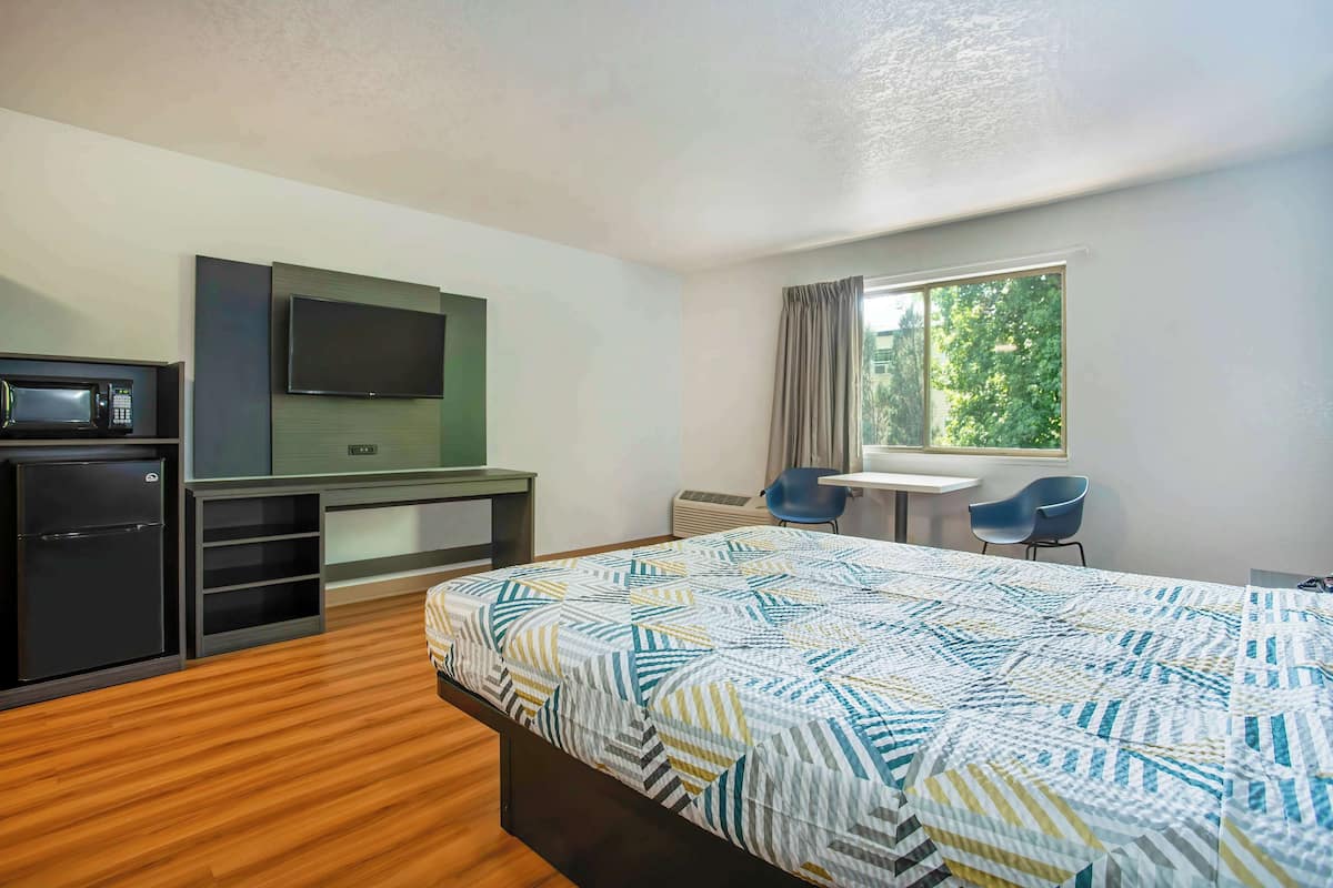 Une chambre d’hôtel avec un lit, un bureau avec une télévision, un four à micro-ondes et une fenêtre avec des rideaux.