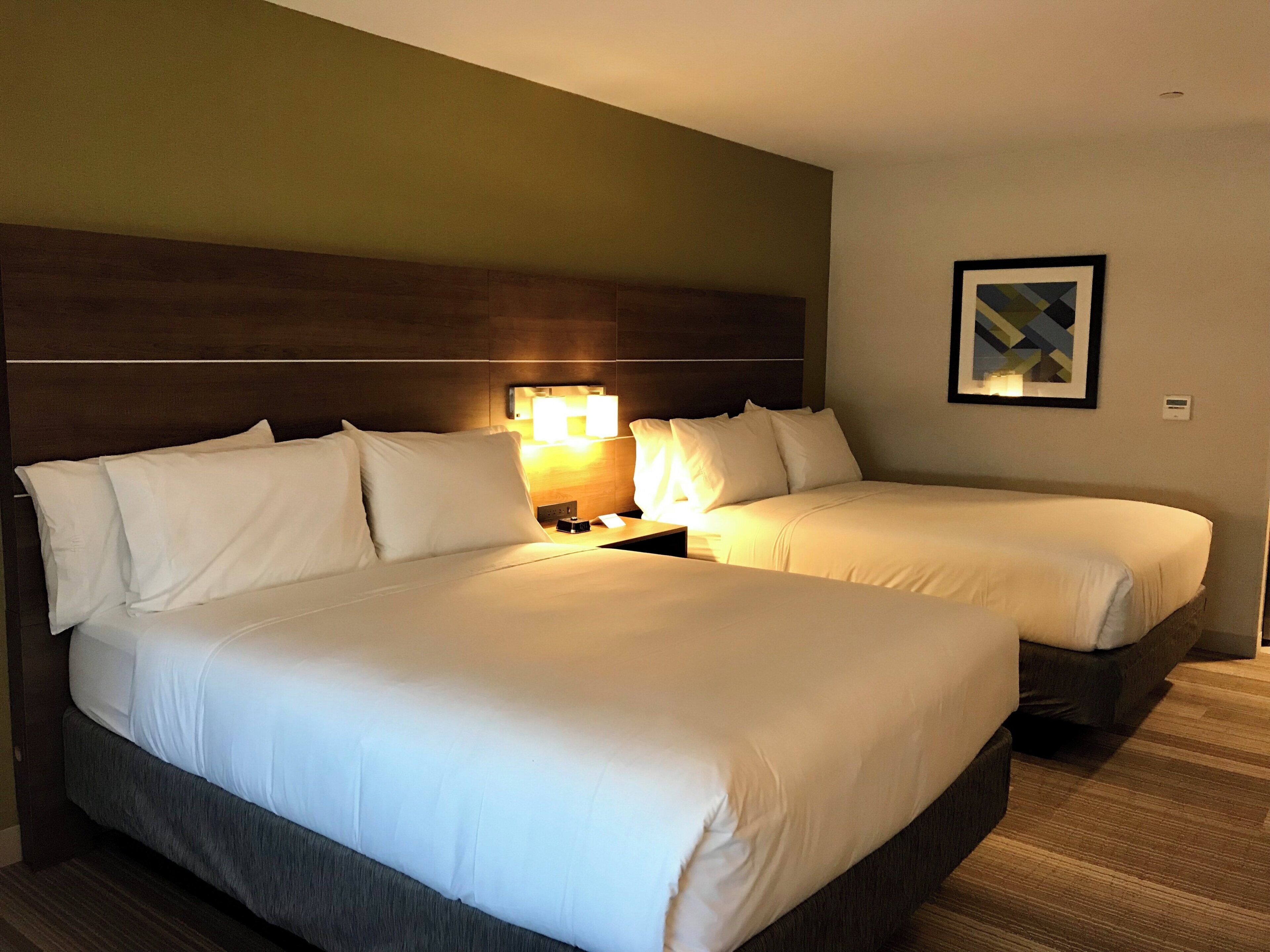 A hotel room with two beds, a nightstand with a lamp, and a framed picture on the wall.