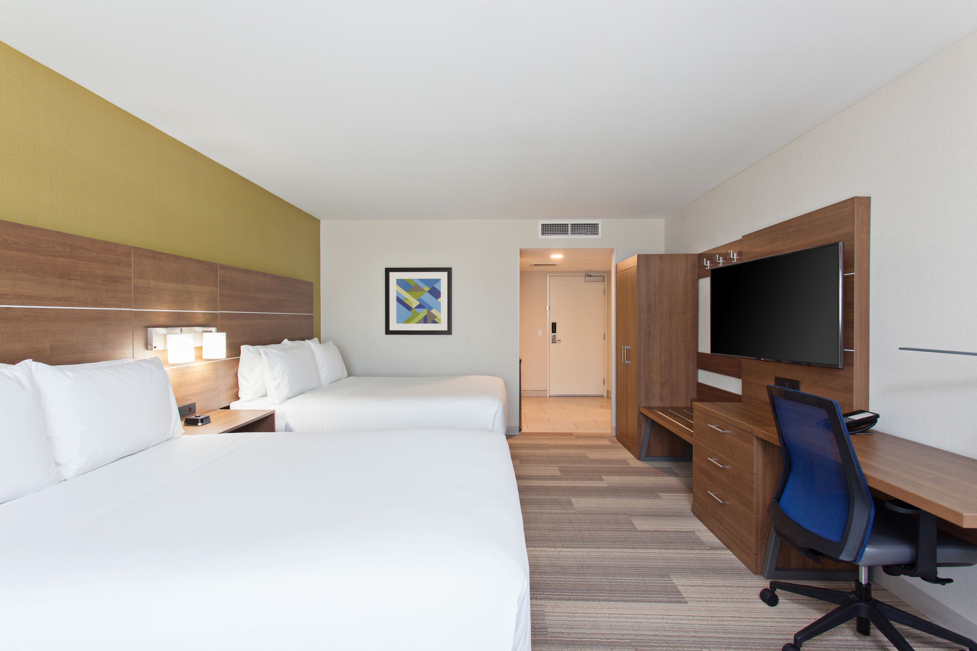 A hotel room with two beds, a desk, a chair, a television, and a framed picture on the wall.
