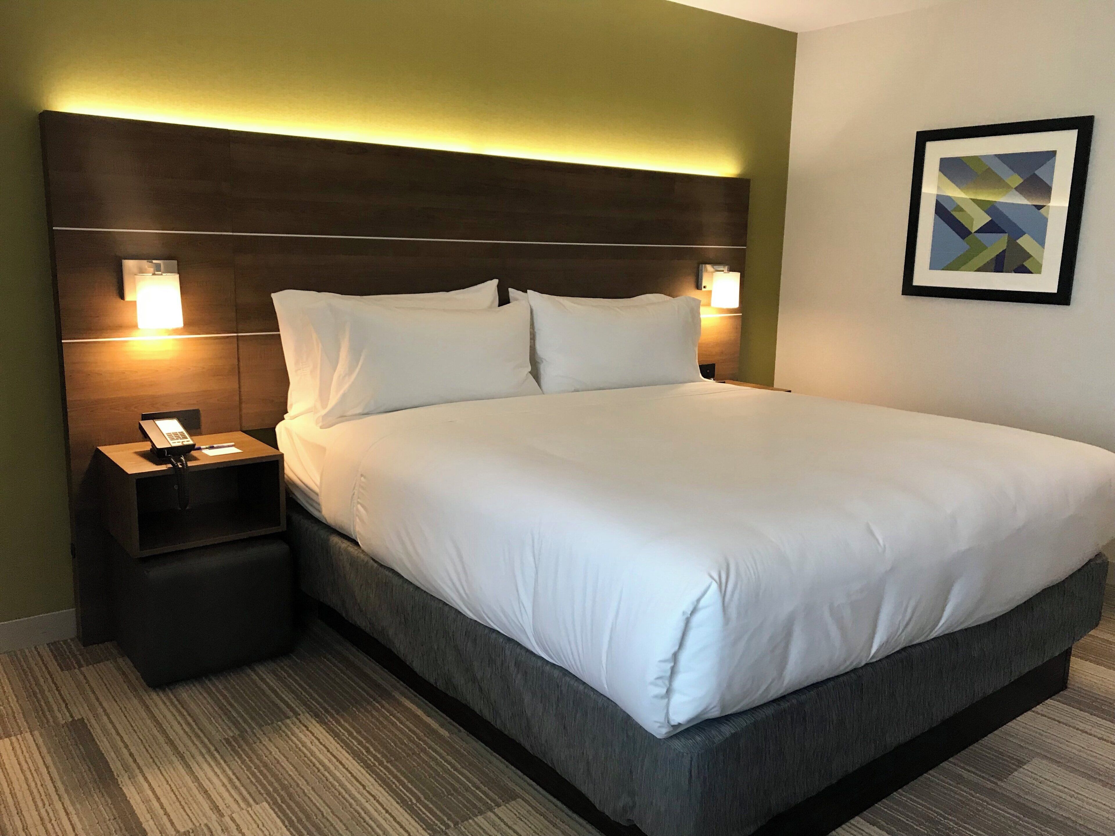 Una habitación de hotel con una cama grande, dos mesitas de noche, un teléfono y una lámpara fijada a la pared.