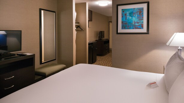 A hotel room with a large bed, a desk with a television, a chair, a small table, and a framed picture on the wall.
