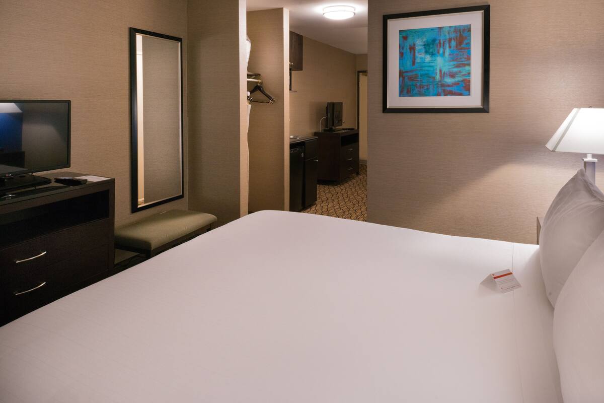A hotel room with a large bed, a desk with a television, a chair, a small table, and a framed picture on the wall.