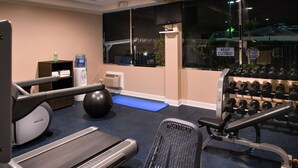 A gym with exercise equipment including a treadmill, a stationary bike, a rowing machine, a bench press, and a set of dumbbells.