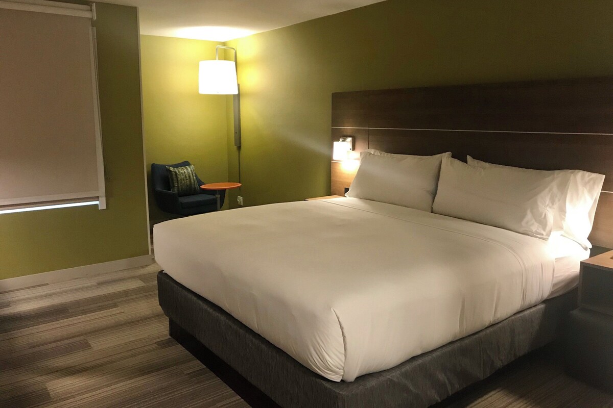 A hotel room with a large bed, a nightstand, a lamp, and a chair.