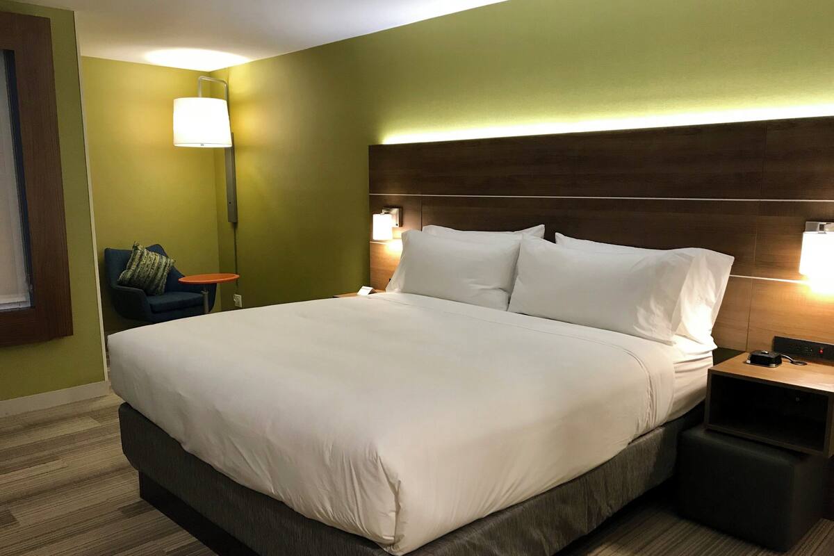 A hotel room with a large bed, a nightstand, a lamp, and a chair.