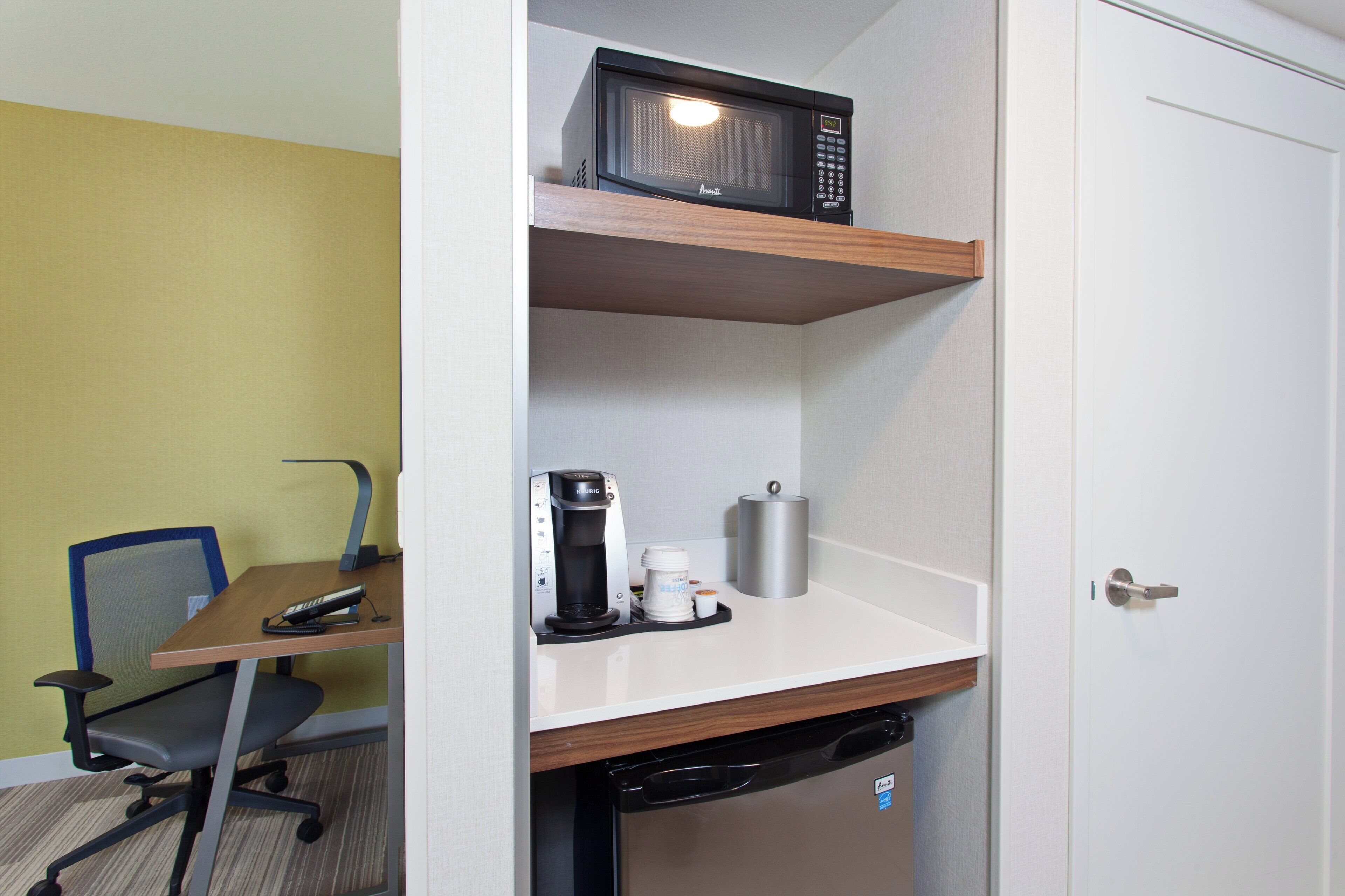 A compact hotel room with a kitchenette, a microwave, a coffee maker, and a small refrigerator.