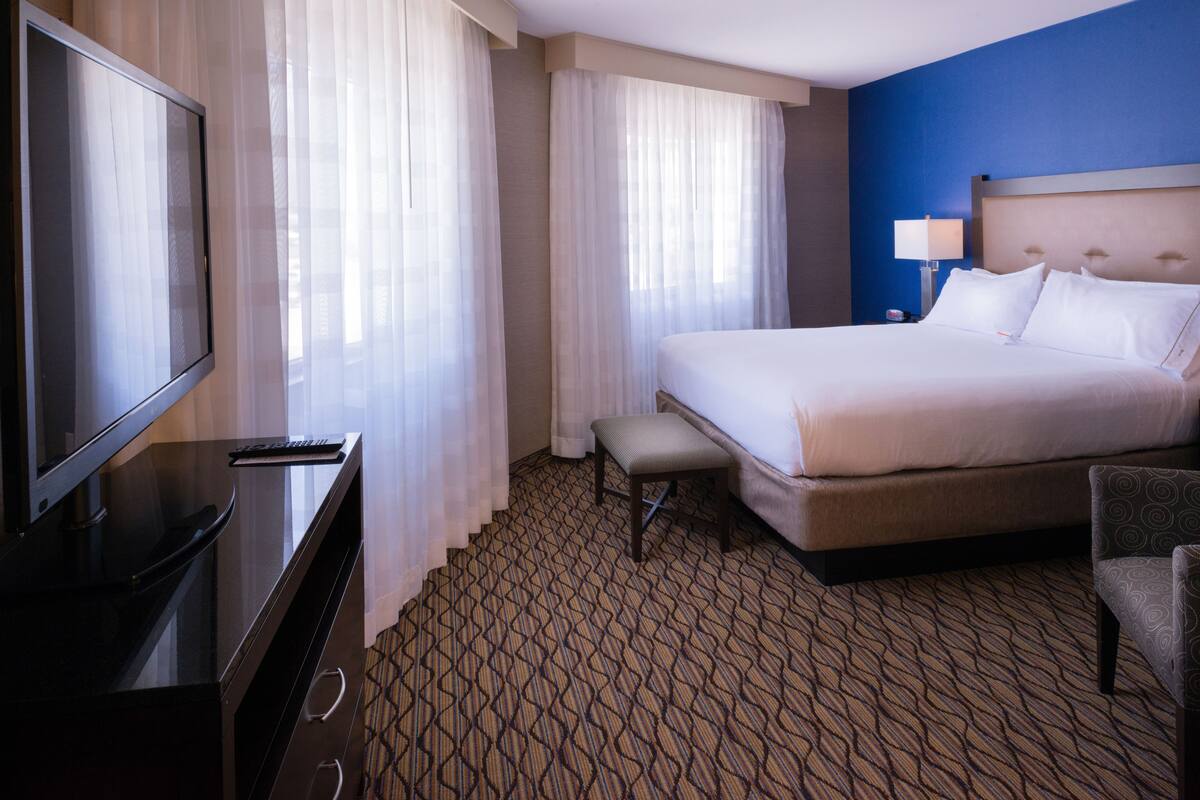 A hotel room with a large bed, a TV, a desk, and a chair.