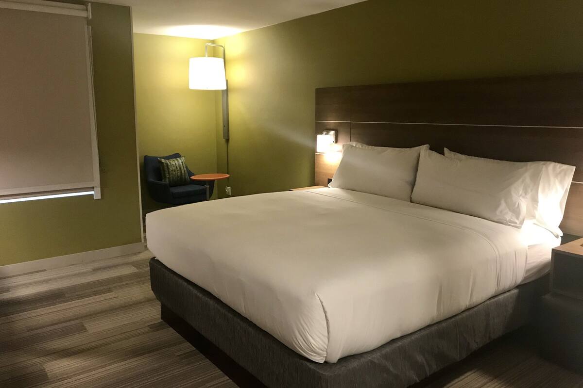 A hotel room with a large bed, a nightstand, a chair, and a small table.