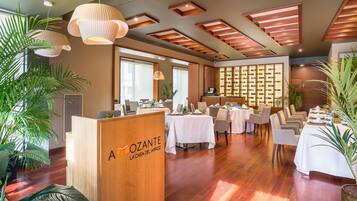A spacious dining area with multiple tables, a reception desk, and a wall of wine bottles.