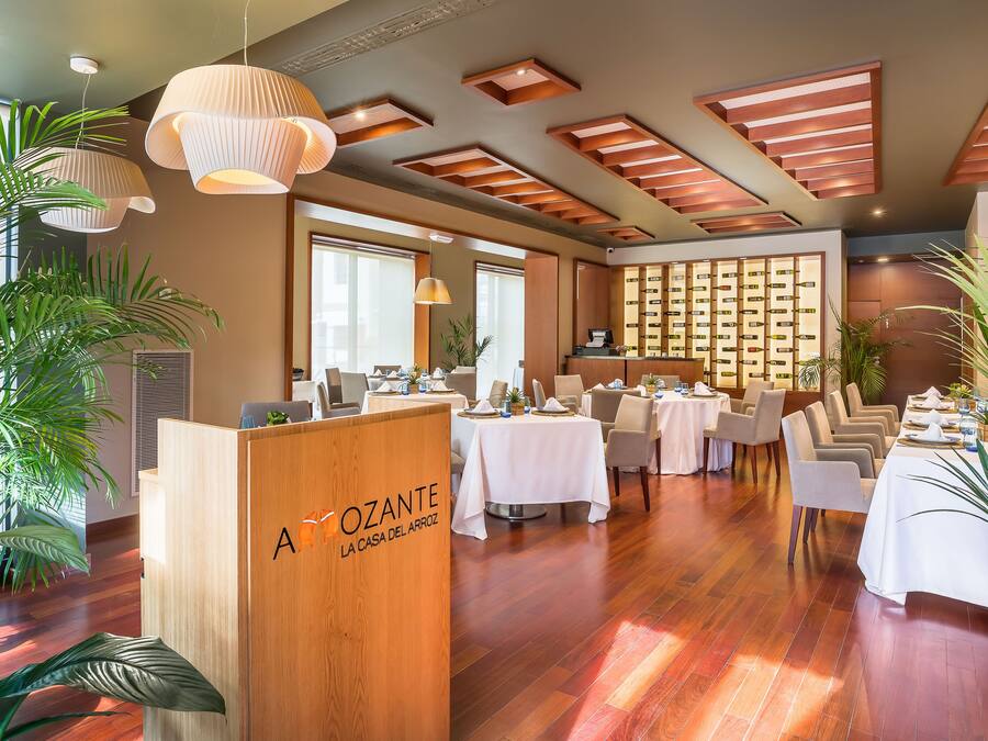 A spacious dining area with multiple tables, a reception desk, and a wall of wine bottles.