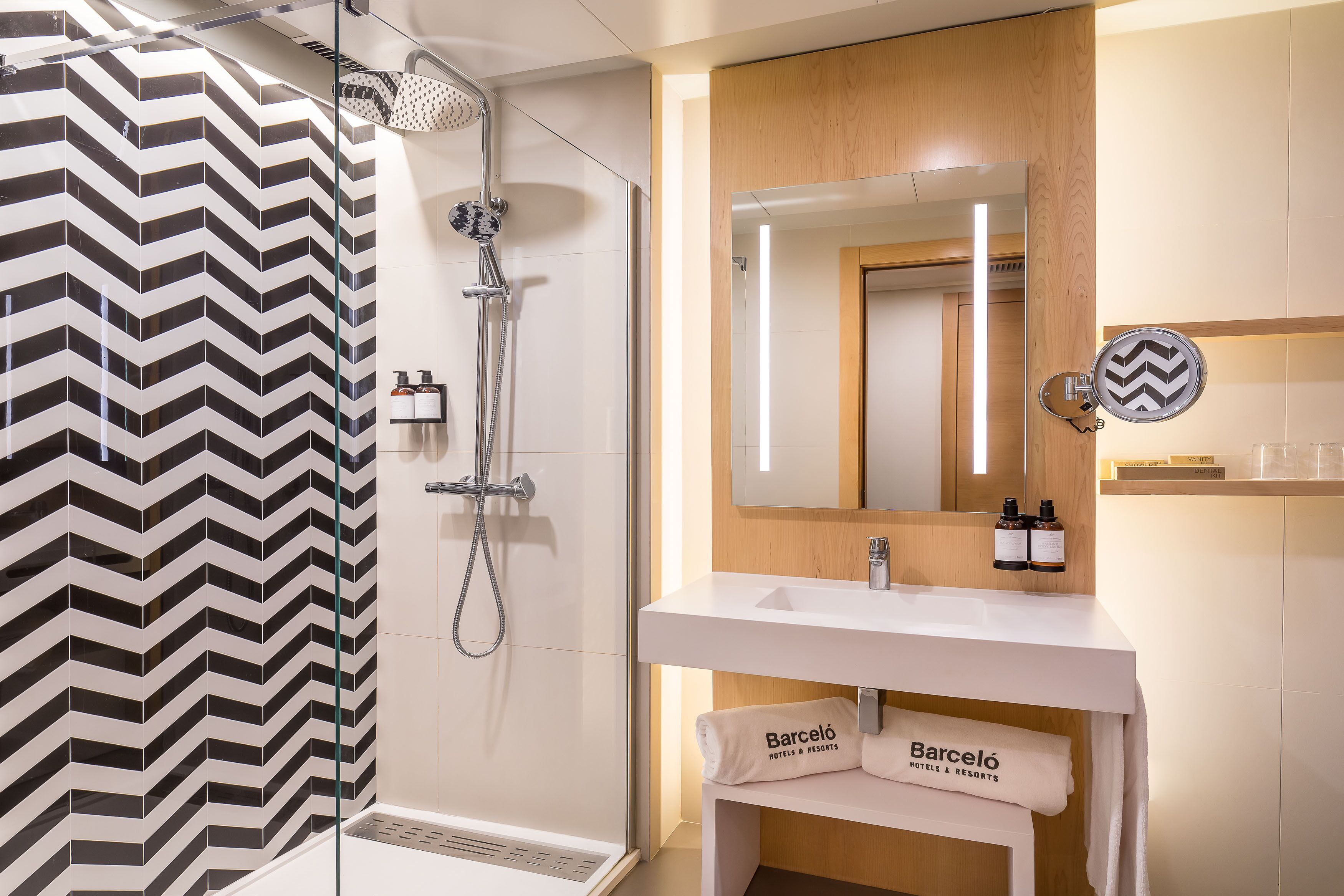 A modern bathroom with a shower, a vanity with a mirror, and a towel rack labeled "Barceló Hotels & Resorts".