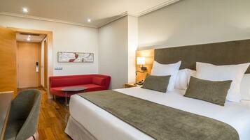 Una habitación de hotel con una cama grande, un sofá rojo, una mesita y una silla.