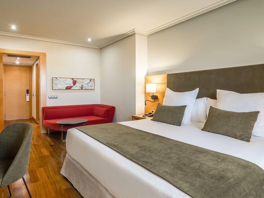 Una habitación de hotel con una cama grande, un sofá rojo, una mesita y una silla.