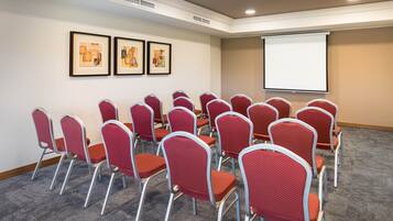 Uma sala de conferências com cadeiras vermelhas e uma tela de projeção.