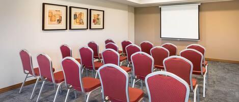 Un salón de conferencias con sillas rojas y una pantalla para proyector.