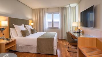 A hotel room with a bed, bedside tables, a desk, a chair, a TV, and a window with curtains.