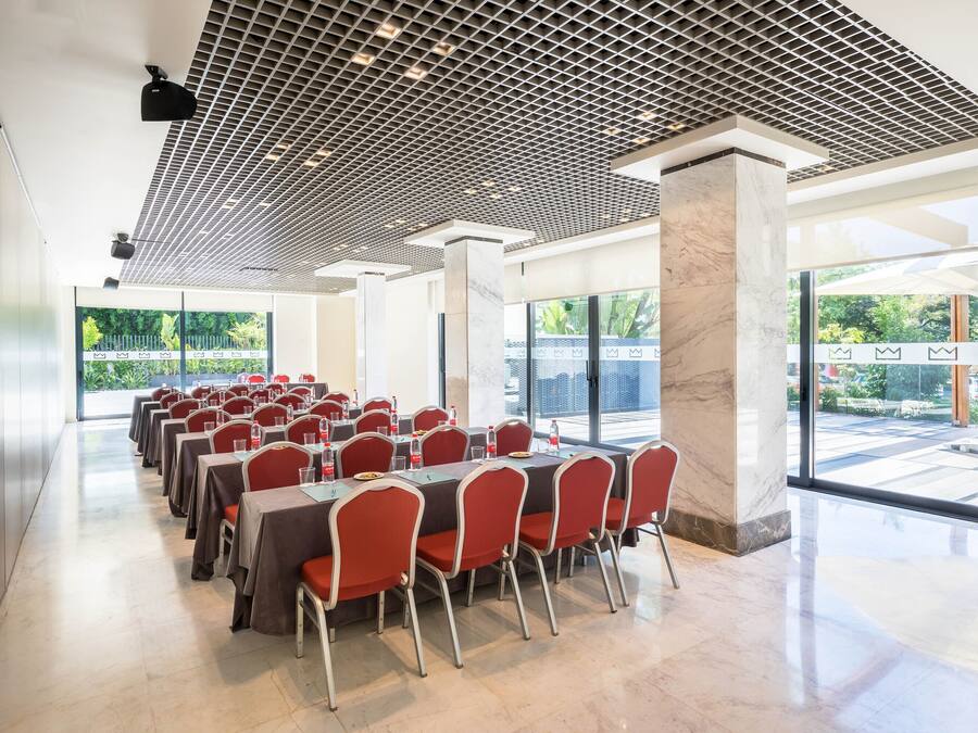 A conference room with rows of tables and chairs, large windows, and a grid-patterned ceiling.
