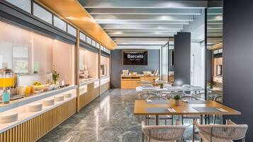 Un moderno vestíbulo de hotel con barra de desayuno, zona de estar y cartel del Barceló Hotel Group.