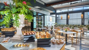 Una cafetería con una variedad de pasteles y postres exhibidos en mesas, rodeada de sillas y plantas en macetas.