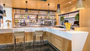 Zona de bar moderna con encimera blanca, dos taburetes y una variedad de botellas.