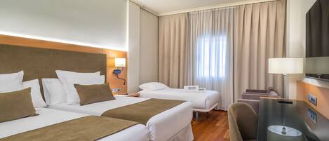 A hotel room with two beds, a desk, a chair, a TV, and a window with curtains.