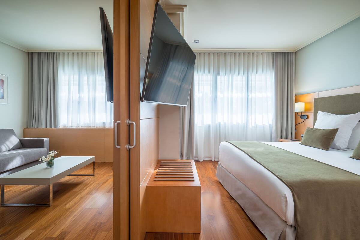 Une chambre d’hôtel avec un lit, un canapé, une télévision et un banc en bois.