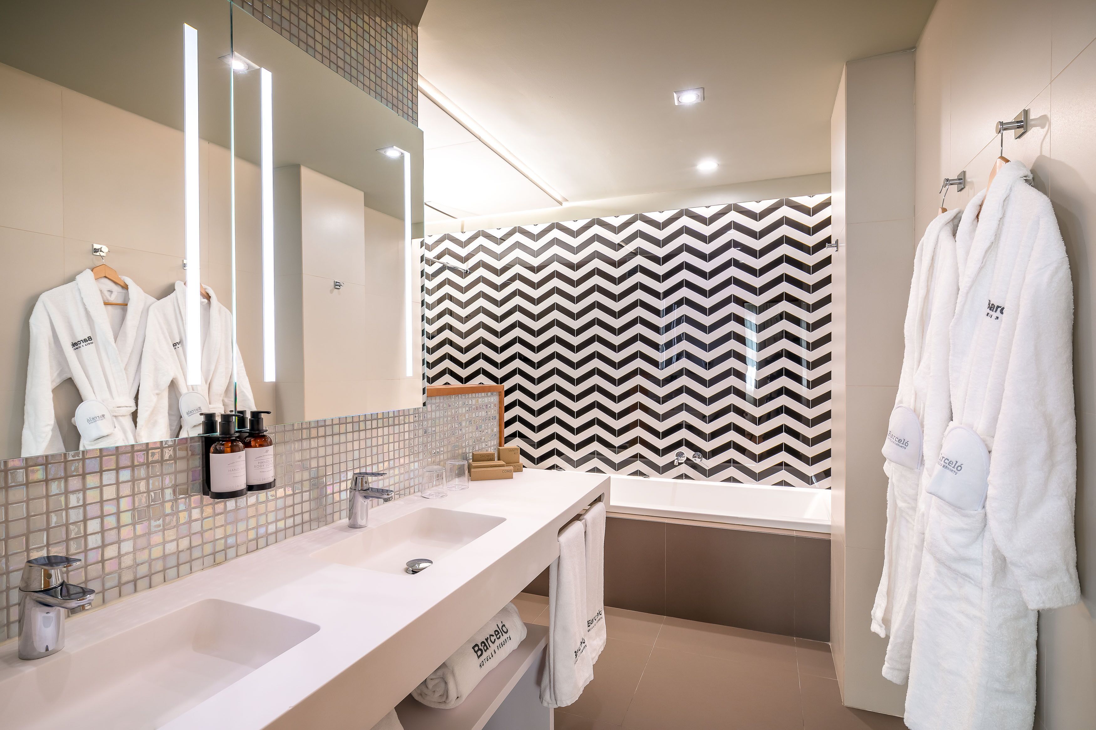 A modern bathroom with two sinks, a large mirror, and a black and white chevron-patterned wall.
