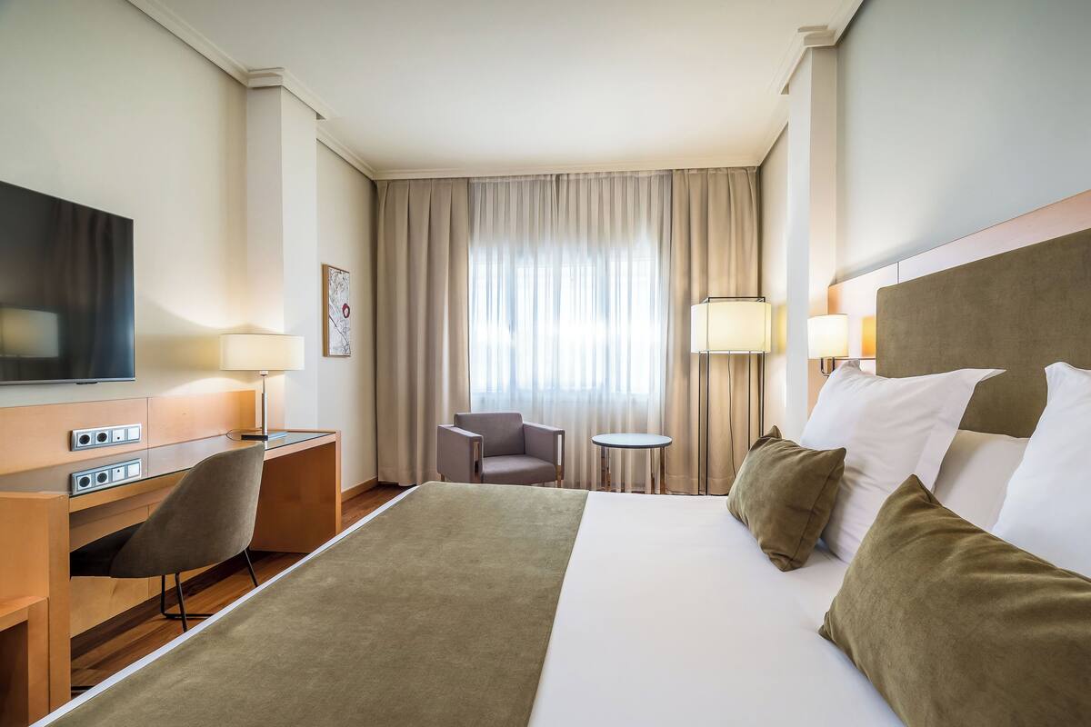 Une chambre d’hôtel équipée d’un lit, d’un bureau, d’une chaise, d’une télévision et d’une fenêtre avec des rideaux.